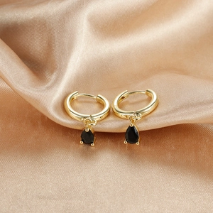 Macro shot of gold hoop earrings with black teardrop zircon on champagne silk background