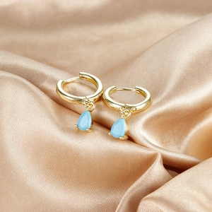 Close-up of golden hoop earrings with light blue teardrop pendants on satin