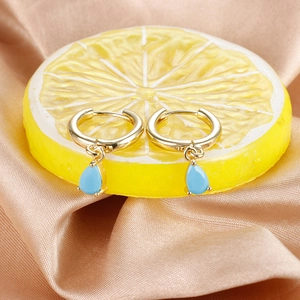 Detail view of gold huggie earrings with light blue waterdrop zircon on silk background