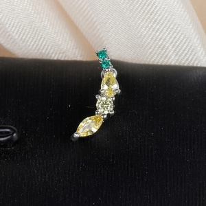 Macro shot of curved silver piercing stud with green and yellow gemstones in claw setting