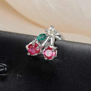Creative cherry fruit stud earring with red and green gems on a textured black surface