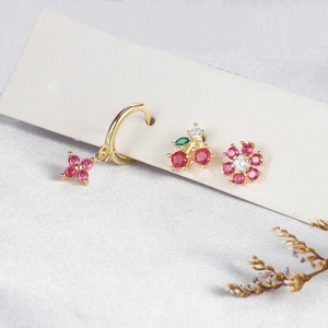 Set di orecchini dorati con fiori rosa e perni a ciliegia su sfondo di seta bianca