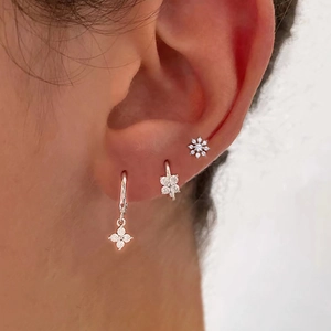 Close-up of sparkling silver zircon flower earrings and studs on a female ear