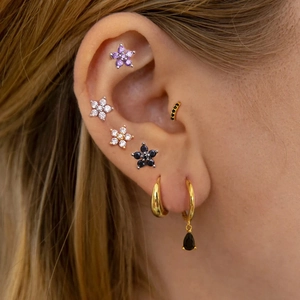 Close-up of assorted stainless steel flower studs and hoop earrings on a female model's ear