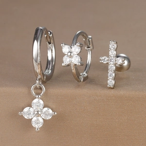 Macro detail of three-piece silver zircon earring set with flower and cross charms