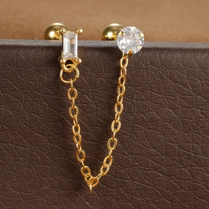 Macro-detail van gouden dubbele piercing oorbel met ketting en heldere zirkoon steen