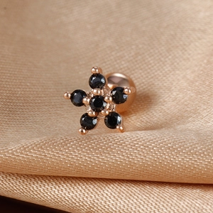 Close-up of rose gold floral piercing stud with black gemstones on champagne silk fabric