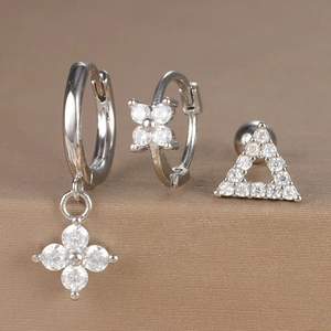 Detail of silver clover earrings set with clear zircon stones on textured background