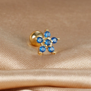 Macro detail of star shaped gold piercing stud with blue crystals on silk fabric