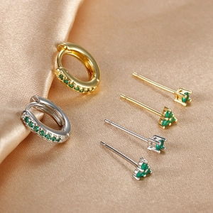 Detalle de set de pendientes de oro y plata con circonitas verdes sobre tela de satén