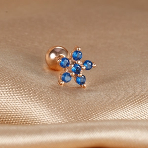 Macro shot of rose gold flower cartilage stud with blue gemstones on champagne silk