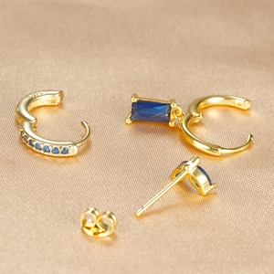 Detalle macro de pendientes de aro dorados con circón azul y grabado de plata S925