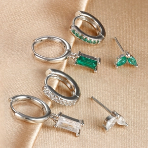 Detalle de pendientes de aro plateados con piedras de circonita verde esmeralda y claras