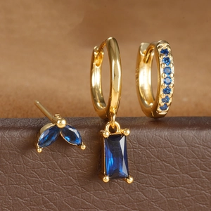 Detalle de set de pendientes dorados con circonitas azul zafiro y formas geométricas