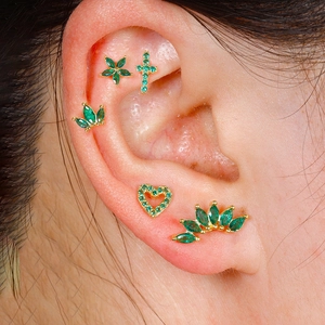 Detailed close-up of five green zircon gold ear studs featuring crown and cross designs