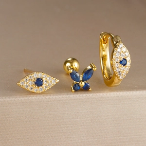 Detalle de 3 pendientes dorados ojo turco y mariposa azul con cristales brillantes