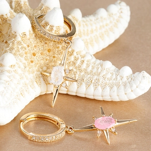 Detailed close-up of gold starburst earrings with white and pink stones on silk