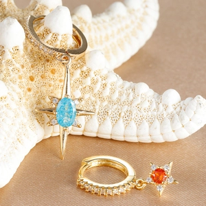 Elegant gold-tone star earrings with blue and orange gems on a warm silk texture