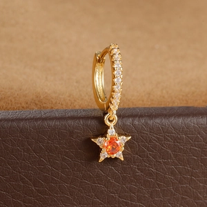 Detalle macro de pendiente de estrella dorada con piedra naranja y circonitas