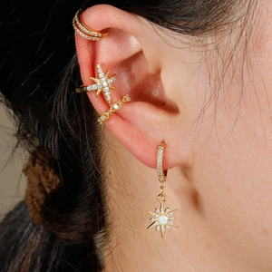 Detalle de pendientes de estrella dorados y ear cuffs con circonitas blancas brillantes