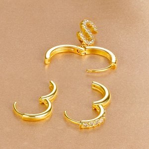 Macro-opname van vergulde oorbellenset met letter S hanger en zirkonia ingelegde ringen