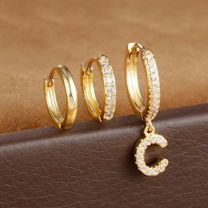 Detail van drie gouden oorringen met zirkonia en een hanger met de letter C