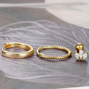 Macro detail of gold twist hoops and marquise zircon crown earring set on textured surface