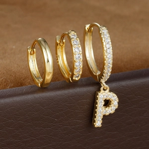 Macro-opname van goudkleurige oorbellen set met gladde ringen en zirkonia letter P hanger set