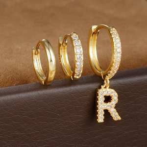 Macro-opname van drie gouden oorbellen met kristallen pavé en letterhanger detail