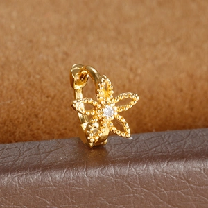 Macro shot of gold floral huggie hoop earring with milgrain detail and zircon center