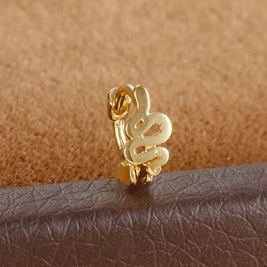 Close-up of a minimalist golden snake-shaped huggie hoop earring on leather stand