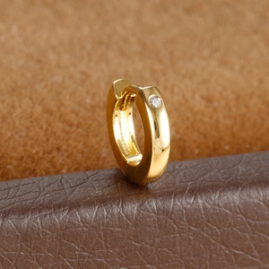 Macro shot of gold huggie hoop earring with a round-cut clear zircon on leather texture