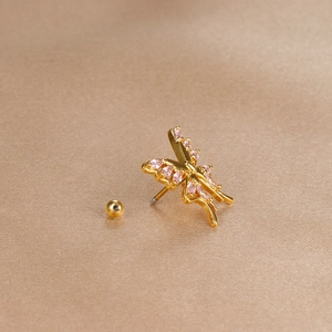 Macro detail of gold-plated butterfly cartilage stud with pink crystal inlays on silk