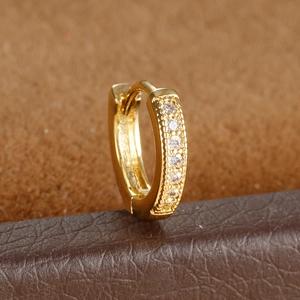 Macro detail of a gold huggie earring with paved white zircons on a leather surface