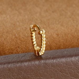 Macro shot of gold twisted rope helix hoop earring on soft textured brown background