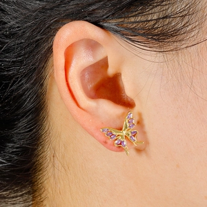 Macro detail of gold-plated butterfly cartilage stud with purple gemstone inlay