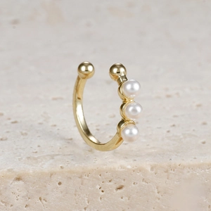 Makro-Detail des eleganten vergoldeten Ear Cuffs mit drei weißen Perlen auf Naturstein