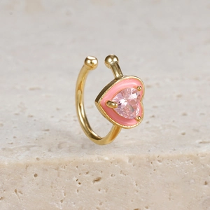 Detail der rosa Herz-Ohrklemme mit Zirkonia-Stein und Gold-Finish auf Steinfläche