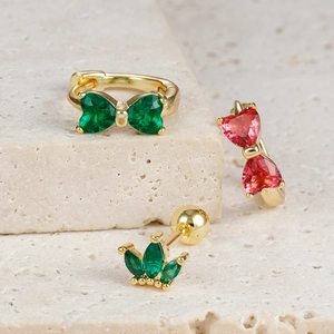 Detailed view of gold bow earrings with green and pink gemstones on stone texture