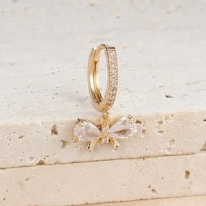 Macro shot of gold bow earrings featuring teardrop zircon crystals on stone background