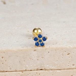 Detail of flower-shaped gold stud earring with blue zircon on beige textured stone