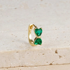Detailed close-up of a gold bow earring with two heart-shaped green cubic zirconia stones
