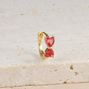 Detailed macro view of 18K gold huggie earring with two red heart-shaped zircon stones