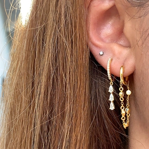 Détail de boucles d'oreilles dorées multicouches avec zircons poire et double chaîne fine