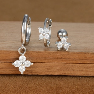 Macro detail of silver clover earrings and zircon stud set on a wooden display stand