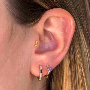 Detailed close-up of gold-plated geometric earrings with zircon and purple flower on ear
