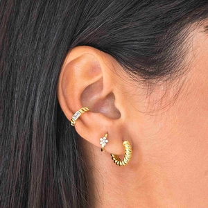 Detail of gold twisted hoop earring and crystal flower stud on a model ear