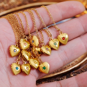 Detail of heart locket necklaces held in hand with starburst engraving and colorful gems