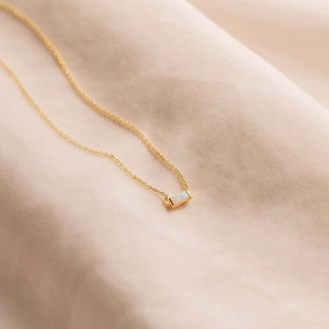 Minimalist gold chain necklace with a rectangular opal pendant on peach fabric