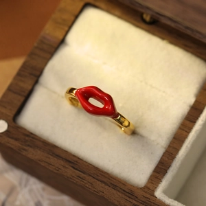 Vue macro d'une bague dorée avec motif lèvres en émail rouge dans un coffret en bois